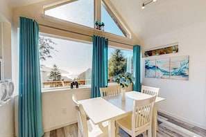 A dining area with a table and chairs, a window with curtains, and a view of trees and mountains.