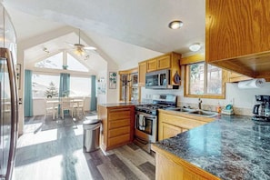 A modern kitchen with wooden cabinets, a granite countertop, and a dining area with a view.