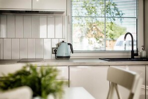 A modern kitchen with white cabinetry, a kettle, and a window with blinds. - Comfortable house with a terrace, sauna, jacuzzi (Niechorze)
