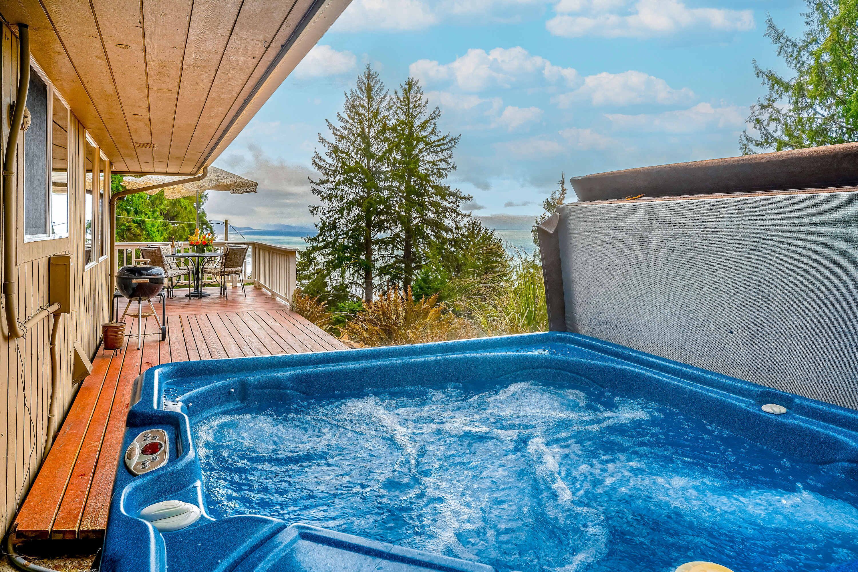 Un jacuzzi en una terraza de madera con vista al océano y árboles.