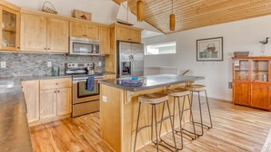 Une cuisine moderne avec des meubles en bois, des appareils en acier inoxydable, un îlot central doté de tabourets et un luminaire suspendu.