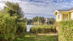 Un quartier résidentiel avec un lac, une végétation luxuriante et une maison jaune dotée d’une terrasse.