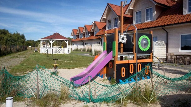 A playground with a slide and climbing structures, surrounded by houses with red roofs. - Luxury holiday home with terrace, sauna, jacuzzi (Niechorze)