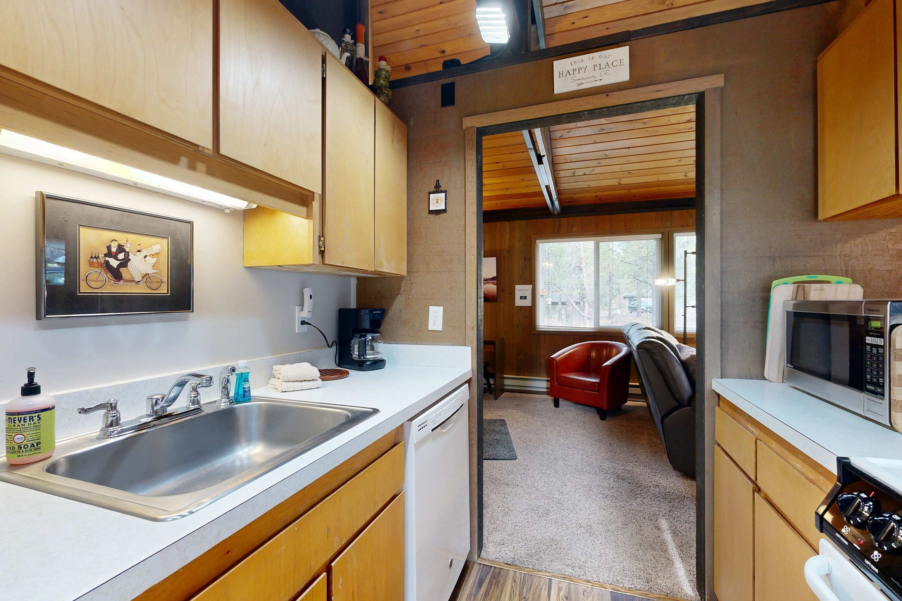 A kitchen with a sink, coffee maker, microwave, and a red chair.