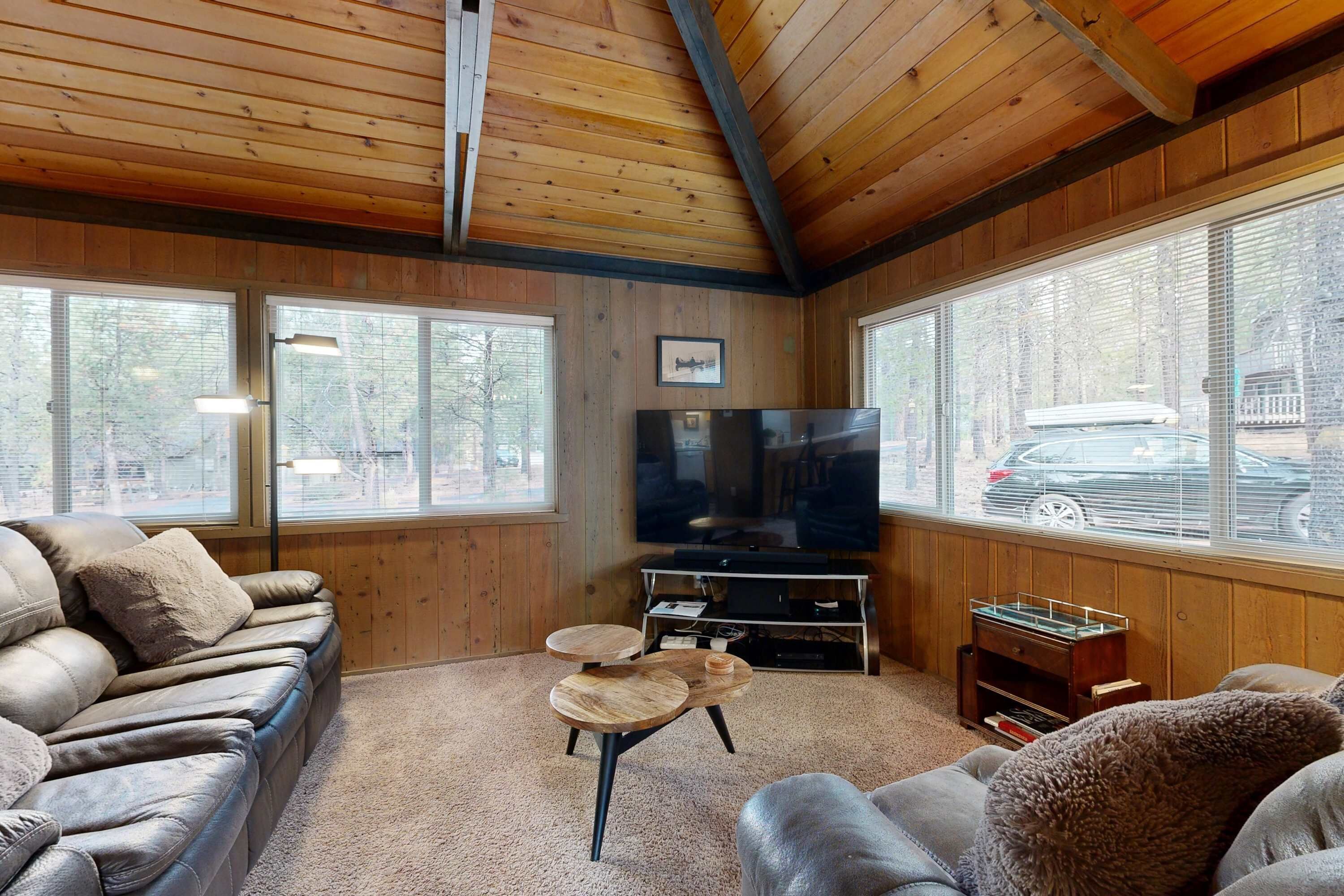 A cozy living room with a leather sofa, a TV, and a large window with a view of the street.
