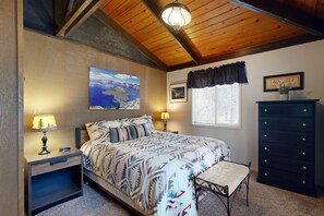 A bedroom with a bed, bedside lamps, a dresser, a window with curtains, and a painting on the wall. - Comfortable Family-Friendly Sunriver Retreat with Deck & Grill - Free SHARC Access (Sunriver)