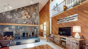 Un salon spacieux avec une cheminée en pierre, un plafond en bois et un téléviseur.