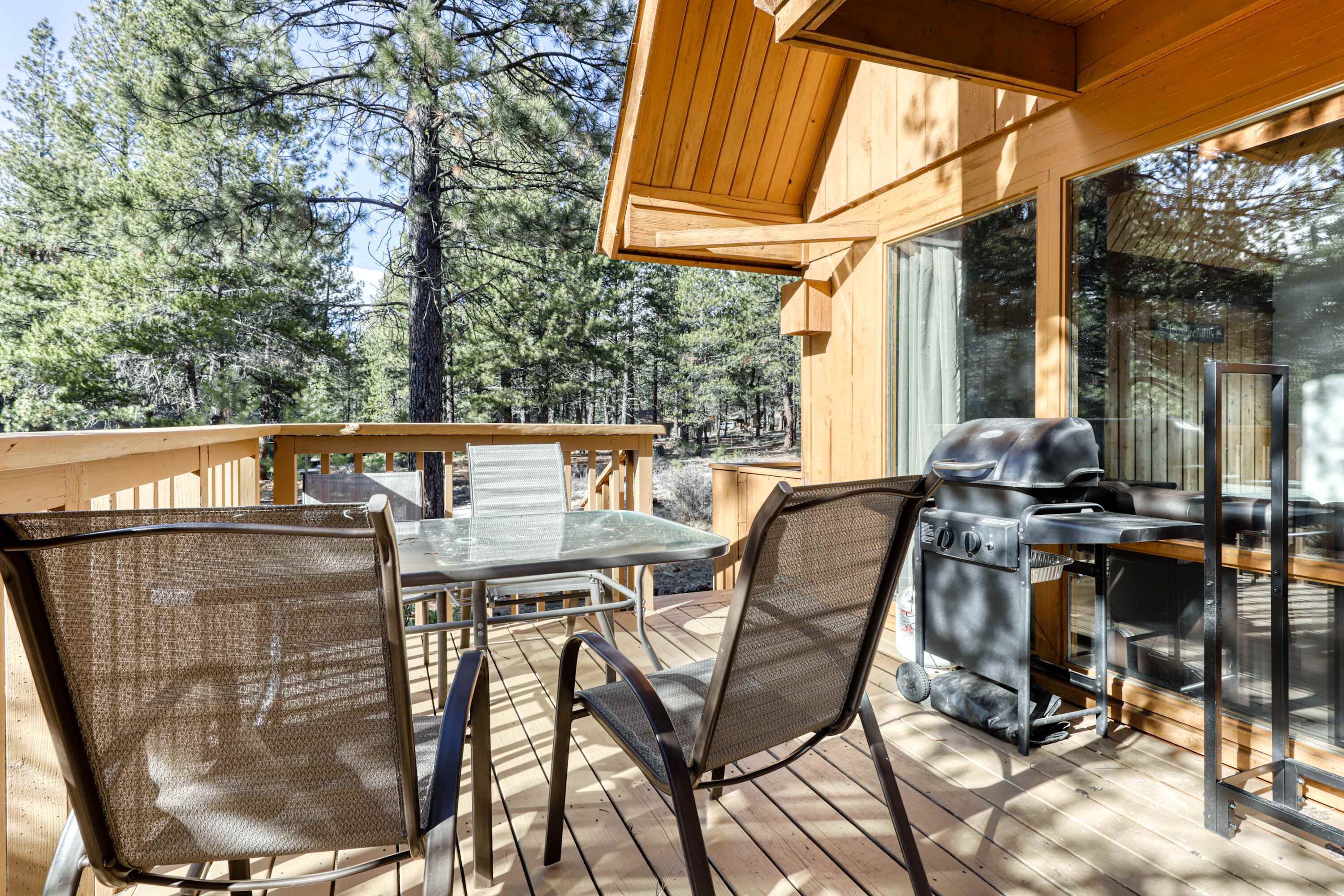 A wooden deck with a table and chairs, a grill, and a view of a forest.