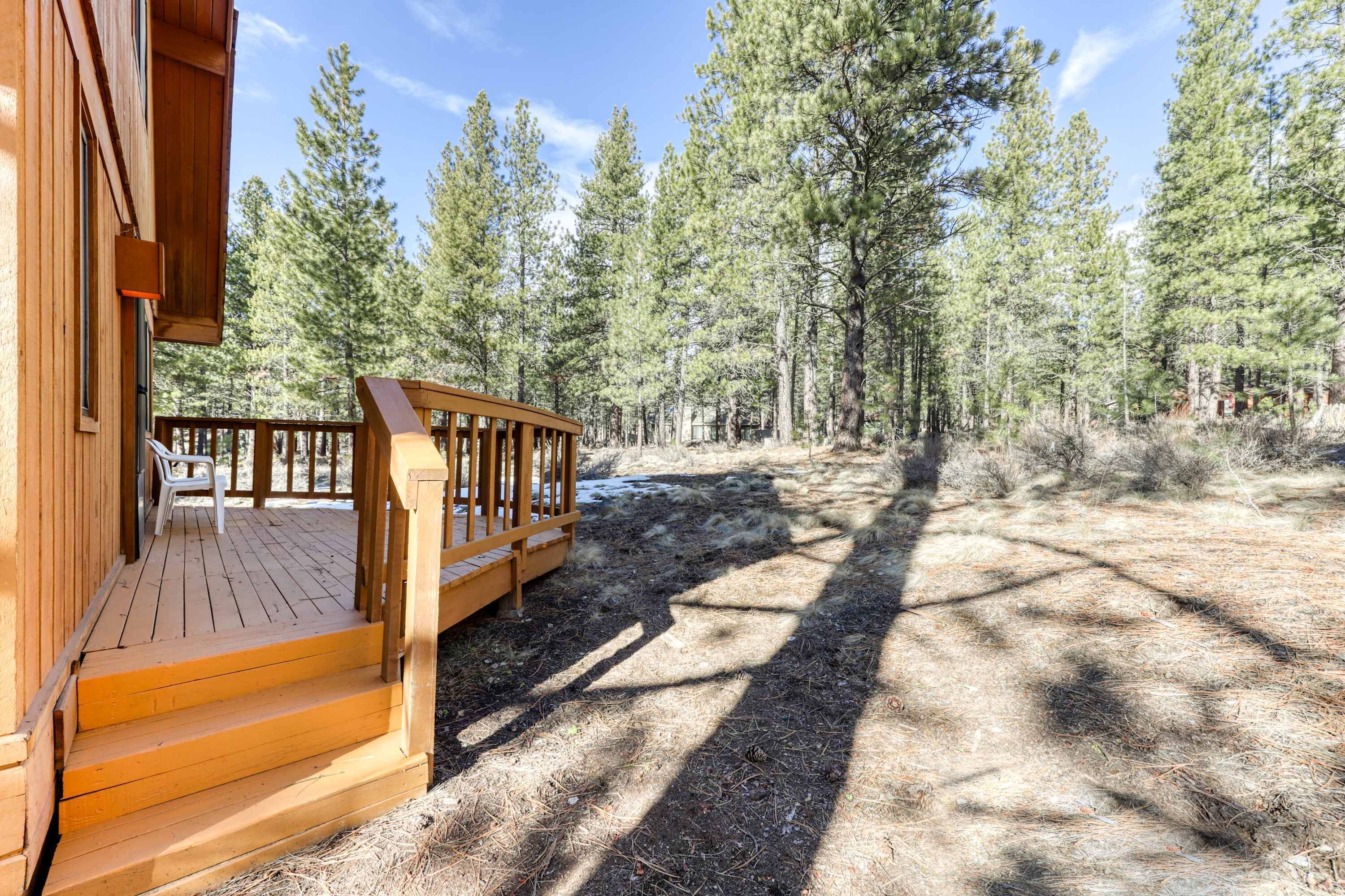 A wooden deck with steps leading to a porch, surrounded by a forested area.