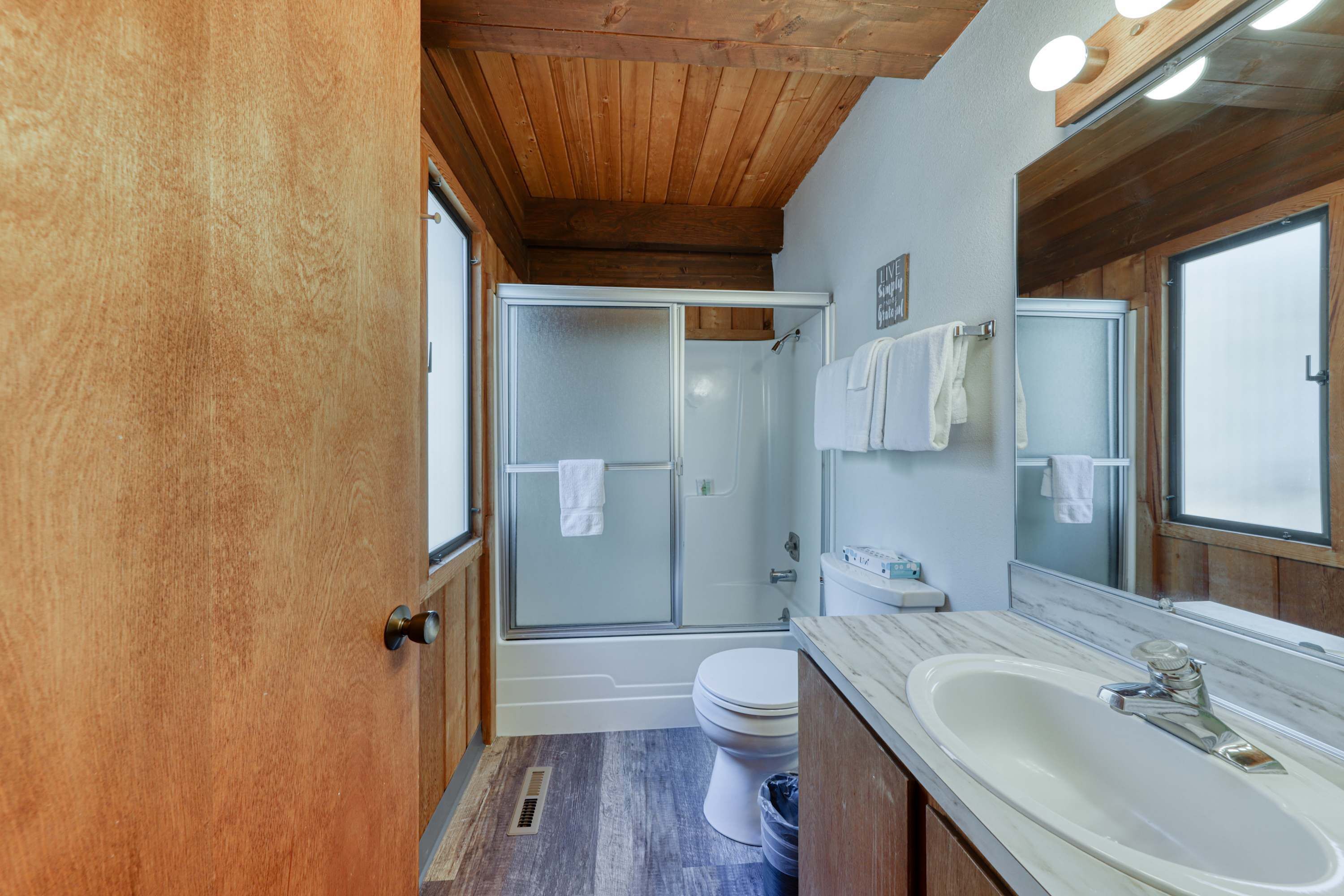 A bathroom with a wooden ceiling, a glass-enclosed shower, a white toilet, and a marble sink.