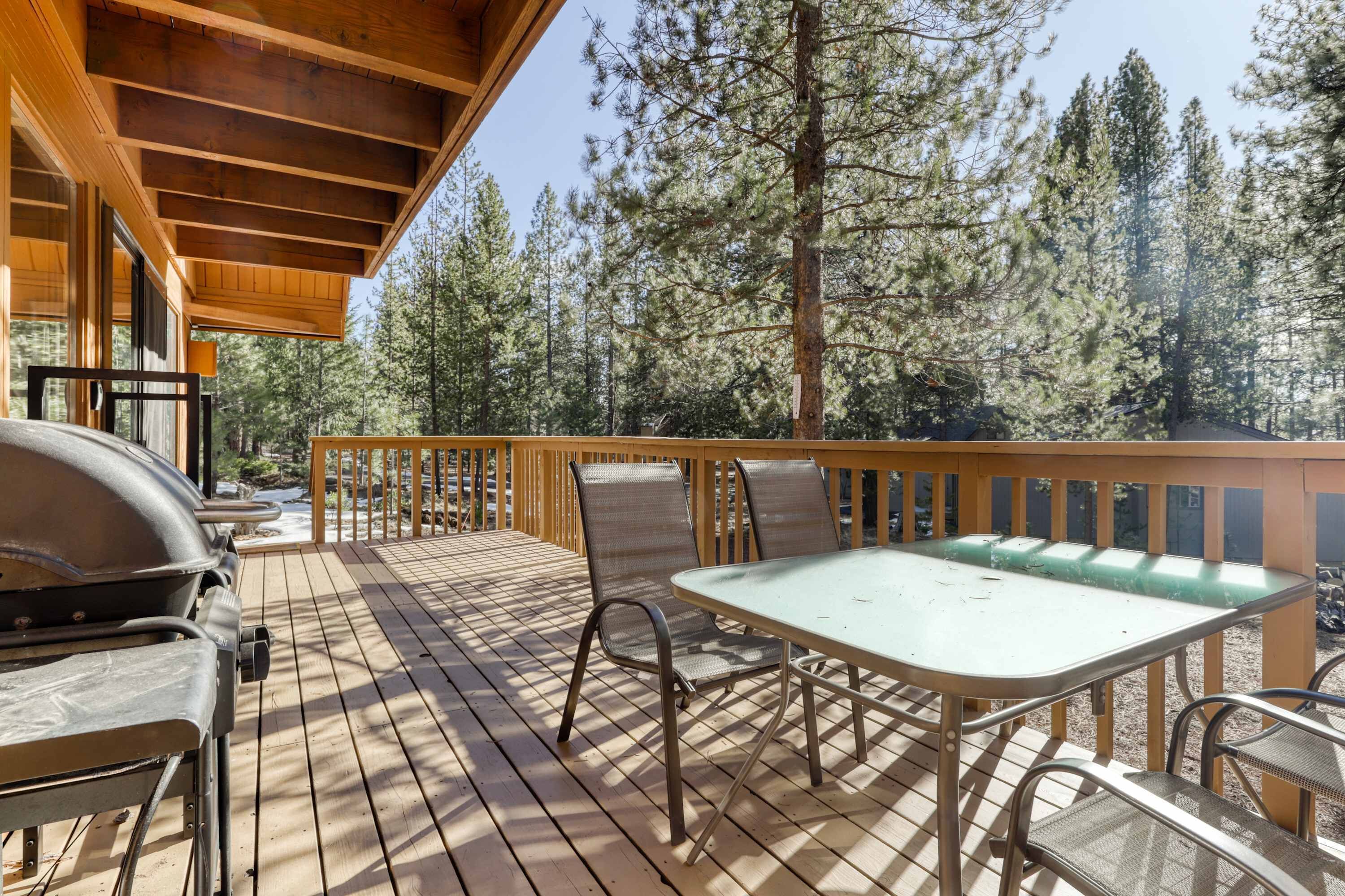 A wooden deck with a table and chairs, surrounded by tall trees.