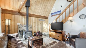 Una sala de estar acogedora con sofá, televisión, chimenea y una escalera.