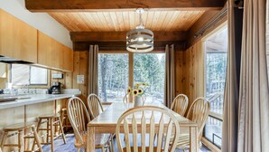 Un interior de madera con una mesa de comedor, sillas, una zona de bar y grandes ventanales.