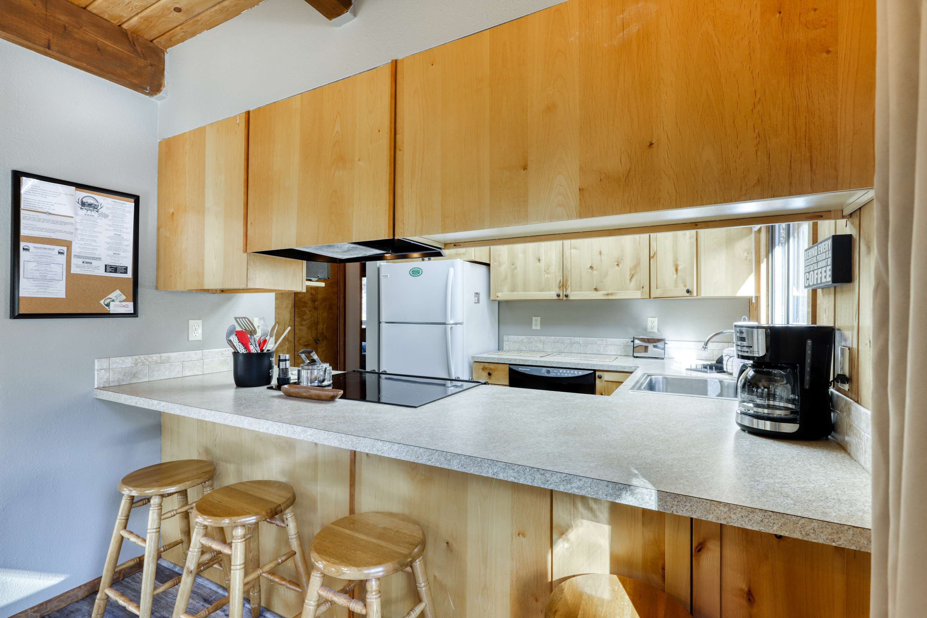 A kitchen with wooden cabinets, a refrigerator, a coffee maker, and two stools.