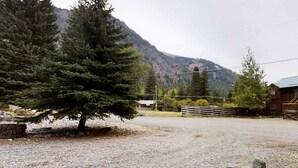 A gravel area with a wooden fence, a building with a green roof, and a mountain in the background. - Wonderful Home Close to Lake withPrivate W&D, WiFi, Gas Fireplace - 2 Dogs Okay (Joseph)