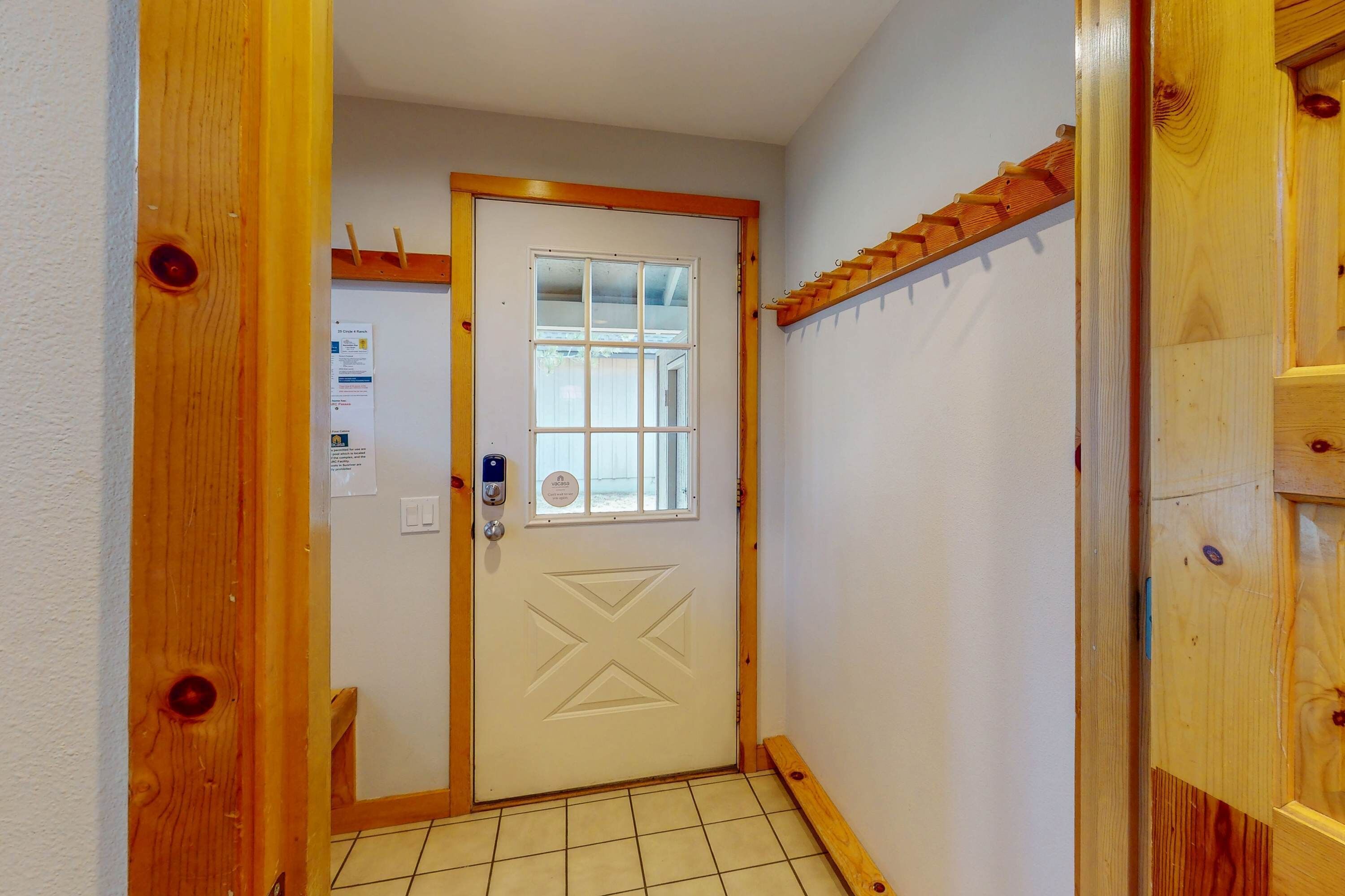 A wooden door with a window, a tiled floor, and a small window with a view of the outside.
