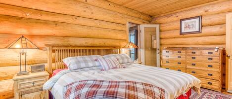 A wooden cabin bedroom with a bed, dresser, nightstand, and a framed picture on the wall.