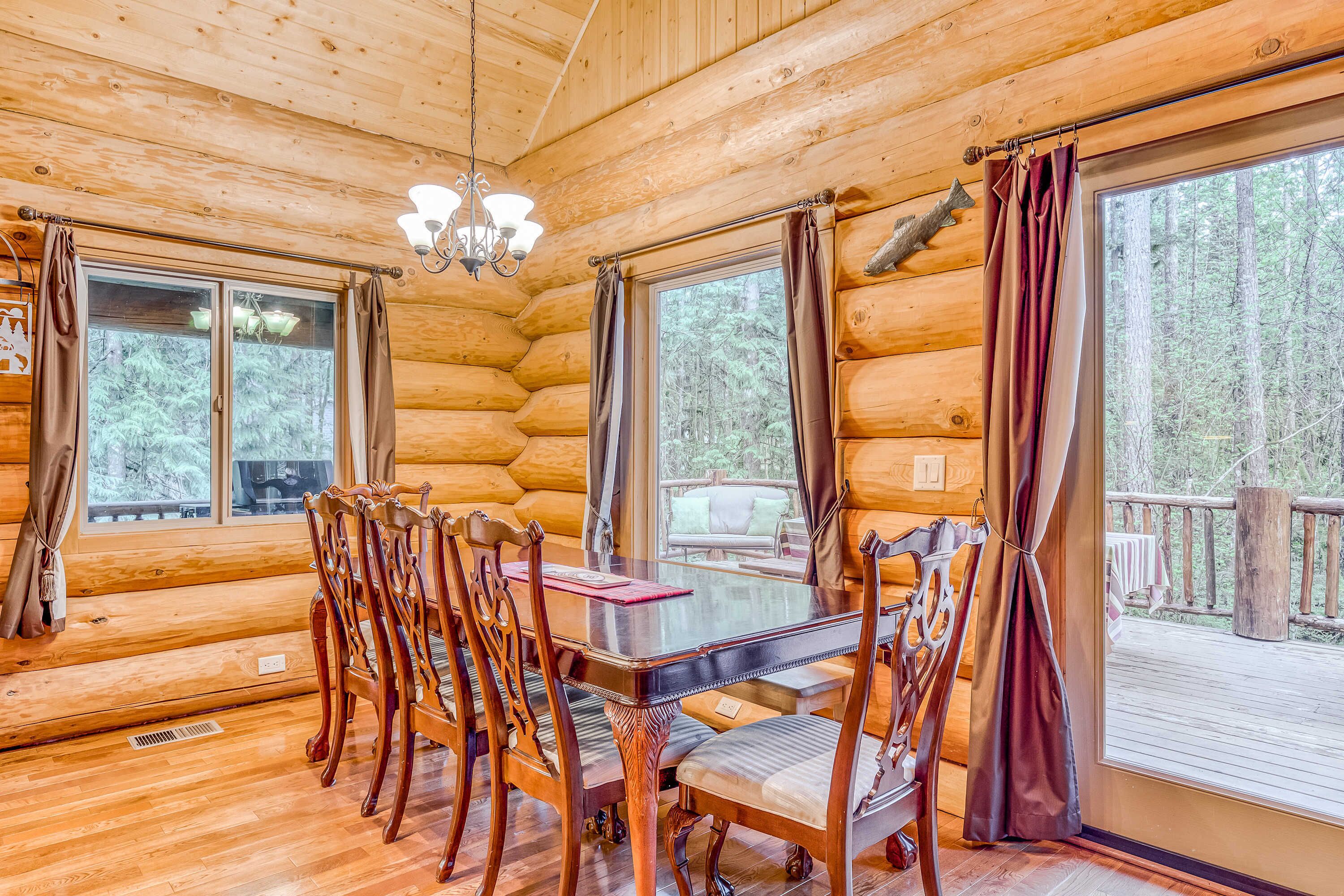 A log cabin interior with a dining table, chairs, and large windows.