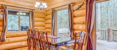 A log cabin interior with a dining table, chairs, and large windows.