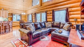 A log cabin interior with a large leather sectional sofa, wooden floors, and large windows. - Woodland home near golf & ski slopes with wraparound deck - dog-friendly (Welches)