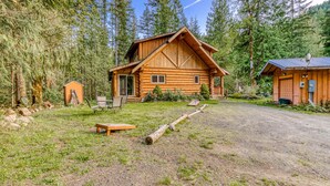 A log cabin with a porch, a small shed, and a gravel driveway. - Woodland home near golf & ski slopes with wraparound deck - dog-friendly (Welches)