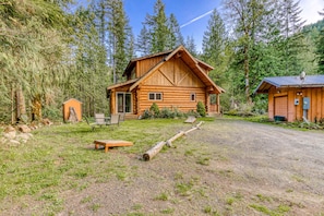 A log cabin with a porch, a small shed, and a gravel driveway.