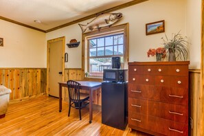 A kitchen with wooden flooring, a dining table with chairs, a refrigerator, a microwave, a cabinet with drawers, a fish mounted on the wall, and a window with a view.