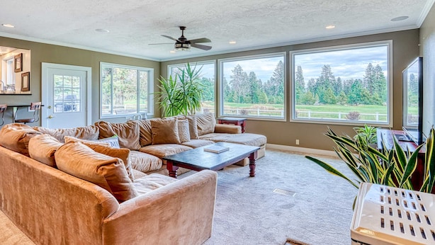 A spacious living room with a sectional sofa, a coffee table, and large windows offering a view of a green landscape. - Spacious Home - Golf Course Views, Central AC, WiFi & Alfresco Living (Bend)