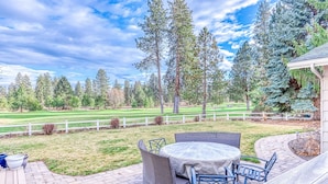 A patio with a round table and chairs, a brick pathway, and a view of a golf course and trees. - Spacious Home - Golf Course Views, Central AC, WiFi & Alfresco Living (Bend)