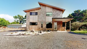 Une maison en bois à deux étages, dotée d’un porche couvert, d’un garage et d’une allée gravillonnée.