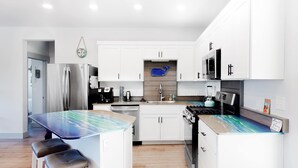 Une cuisine moderne avec des meubles blancs, un îlot central, des appareils en acier inoxydable et un pare-feu bleu.