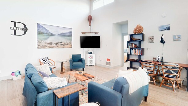 Un salon spacieux doté d’un grand téléviseur à écran plat, d’un coin salon confortable avec des canapés bleus, d’une table basse en bois et d’une bibliothèque.