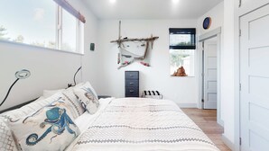 Une chambre à coucher comprenant un lit, une commode, une étagère fixée au mur et une fenêtre.