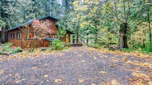 A cabin with a gravel driveway, surrounded by trees and a forest. - Charming Home with Free WiFi, washer&dryer, Wood Fireplace, and Furnished Deck (Sandy)
