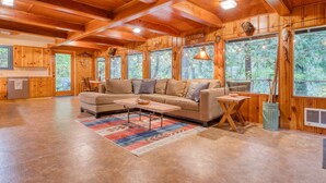 A wooden cabin interior with a sofa, coffee table, and large windows. - Charming Home with Free WiFi, washer&dryer, Wood Fireplace, and Furnished Deck (Sandy)