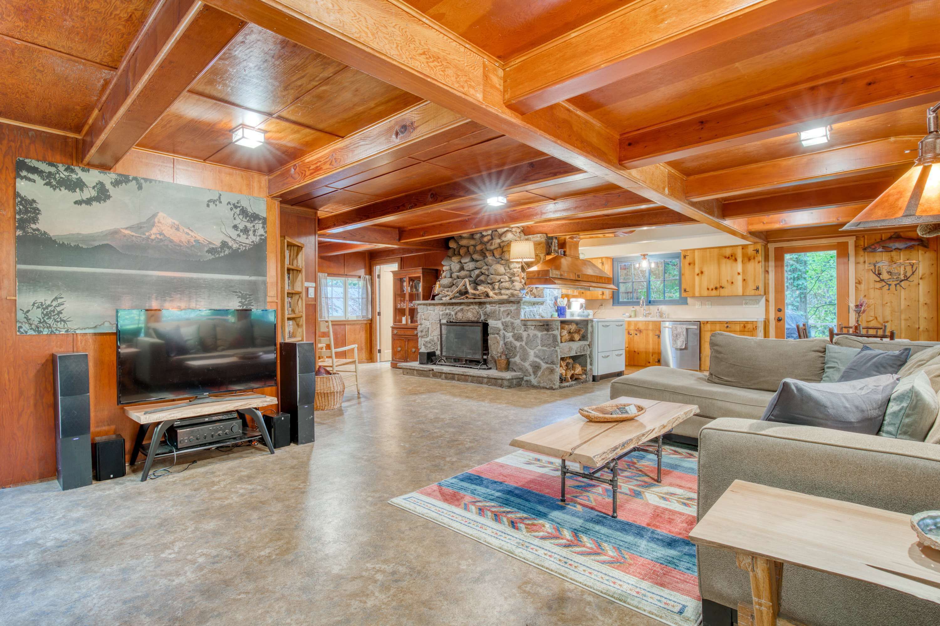 A spacious living area with a stone fireplace, wooden ceiling beams, and a large flat-screen TV.