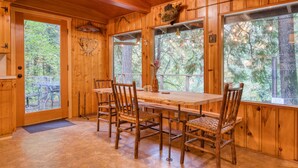 A wooden interior with a dining table and chairs, large windows, and a door leading outside. - Charming Home with Free WiFi, washer&dryer, Wood Fireplace, and Furnished Deck (Sandy)