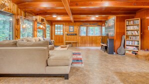 A wooden interior with a sofa, a bookshelf, and a guitar. - Charming Home with Free WiFi, washer&dryer, Wood Fireplace, and Furnished Deck (Sandy)