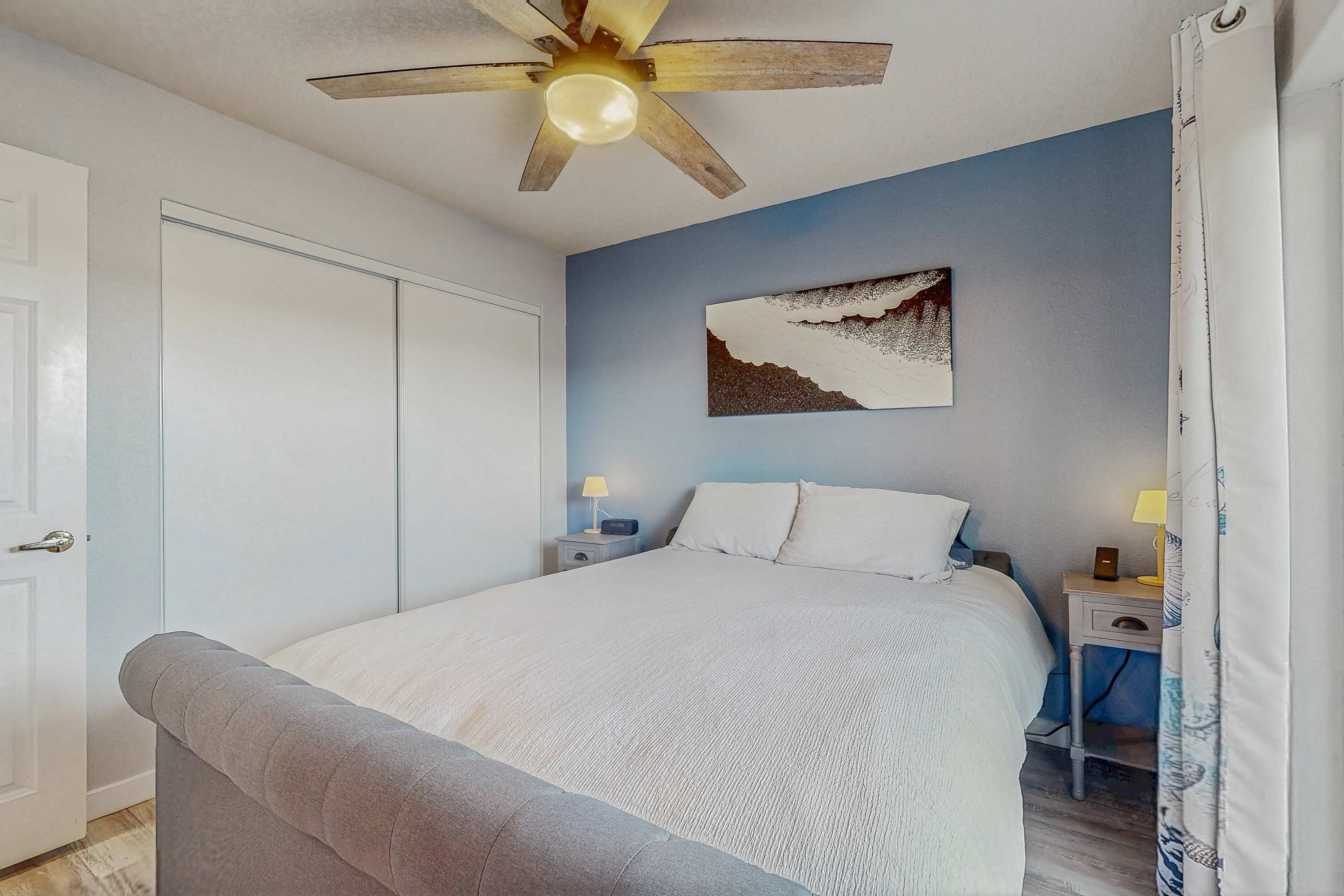 Une chambre à coucher comprenant un lit, un ventilateur de plafond, une table de chevet avec une lampe et une œuvre d’art accrochée au mur.