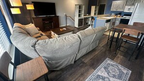 A living room with a sofa, coffee table, TV, and a kitchen area with cabinets and a dining table. - Family Friendly Coastal Getaway Townhome Near Beach & Downtown (Long Beach)