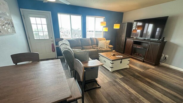 A living room with a sofa, a dining table, a kitchen area with a TV, and large windows. - Family Friendly Coastal Getaway Townhome Near Beach & Downtown (Long Beach)
