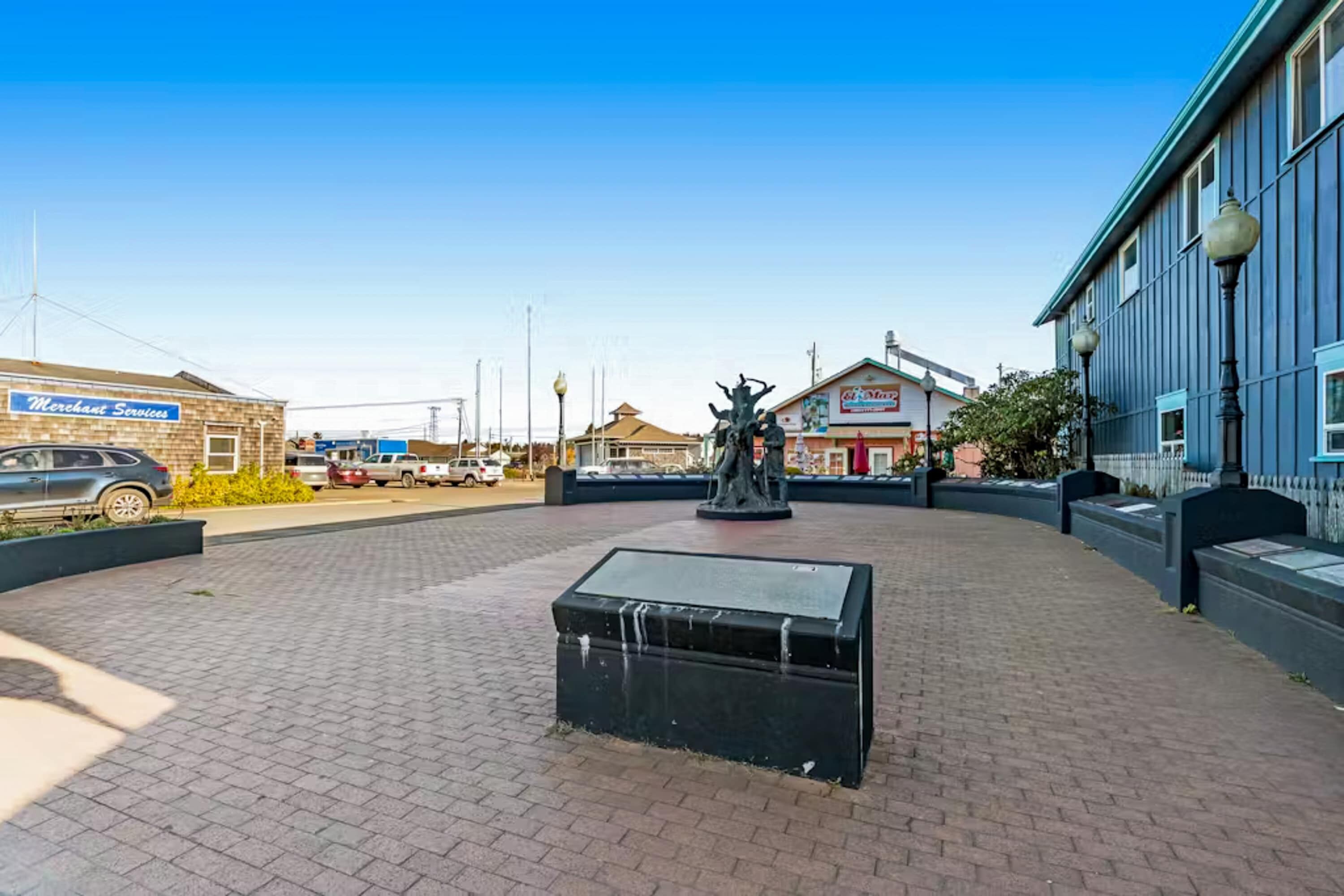 A paved plaza with a statue, a building labeled 'Merchant Services,' and another building with a sign.