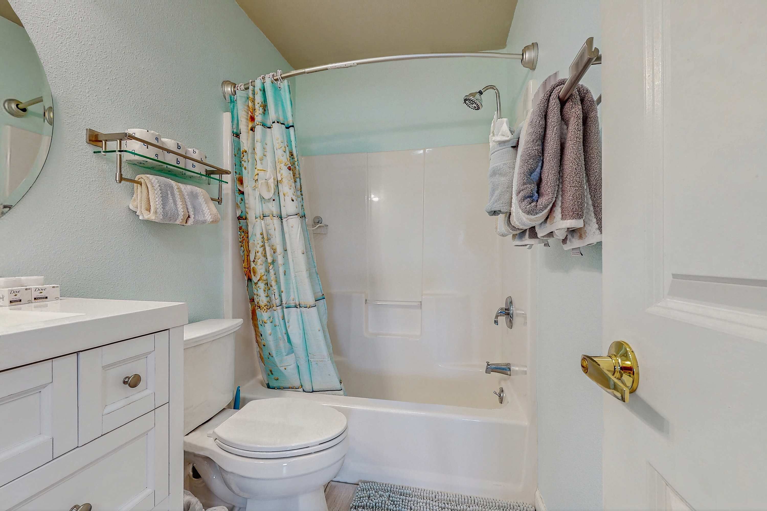 Ein Badezimmer mit Toilette, Badewanne, Duschvorhang, Handtuchhalter und einem Waschtisch mit Spiegel.
