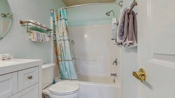Ein Badezimmer mit Toilette, Badewanne, Duschvorhang, Handtuchhalter und einem Waschtisch mit Spiegel.