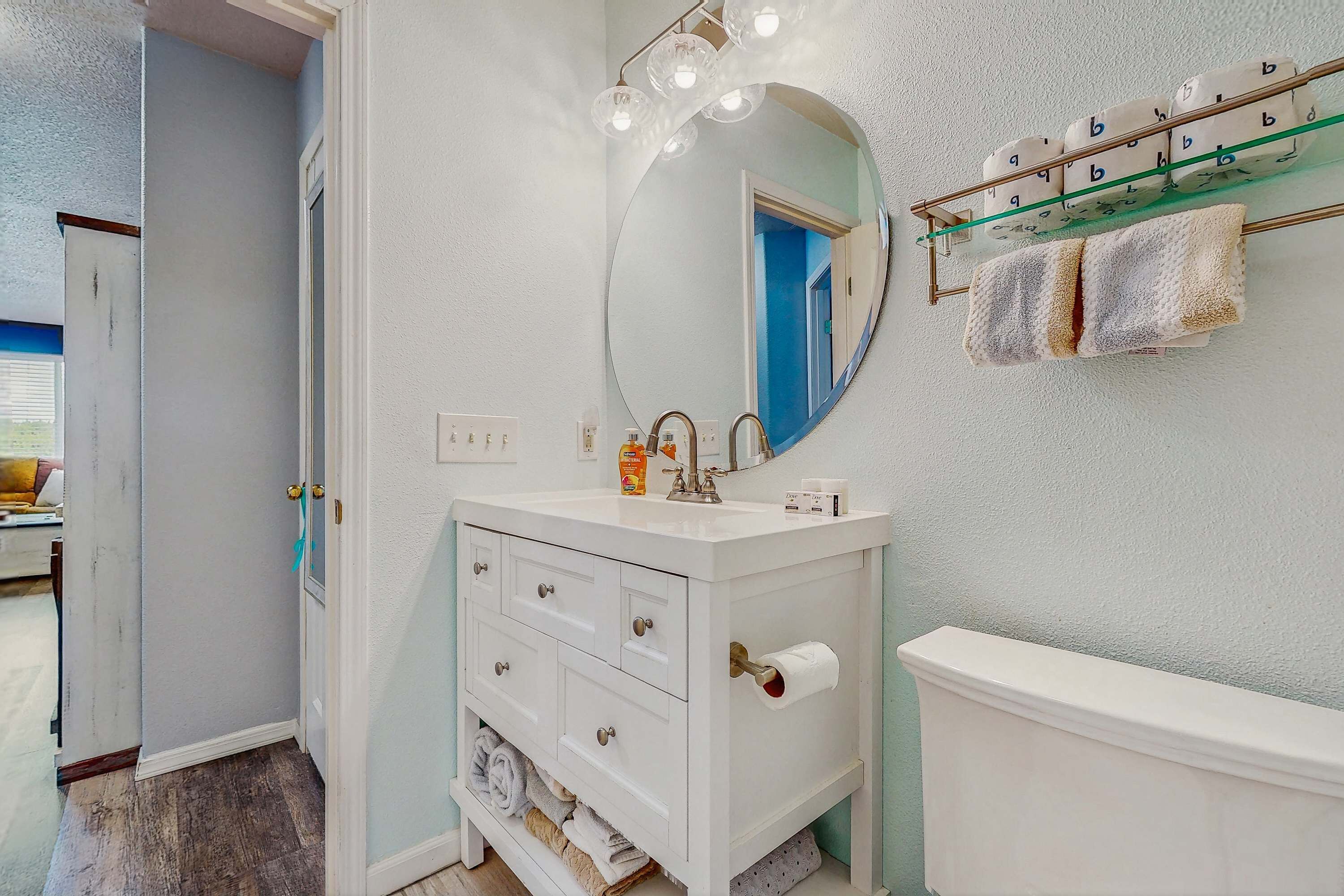 Un bagno con un mobile lavabo bianco, uno specchio rotondo, un appendi asciugamani e un porta rotolo di carta igienica.