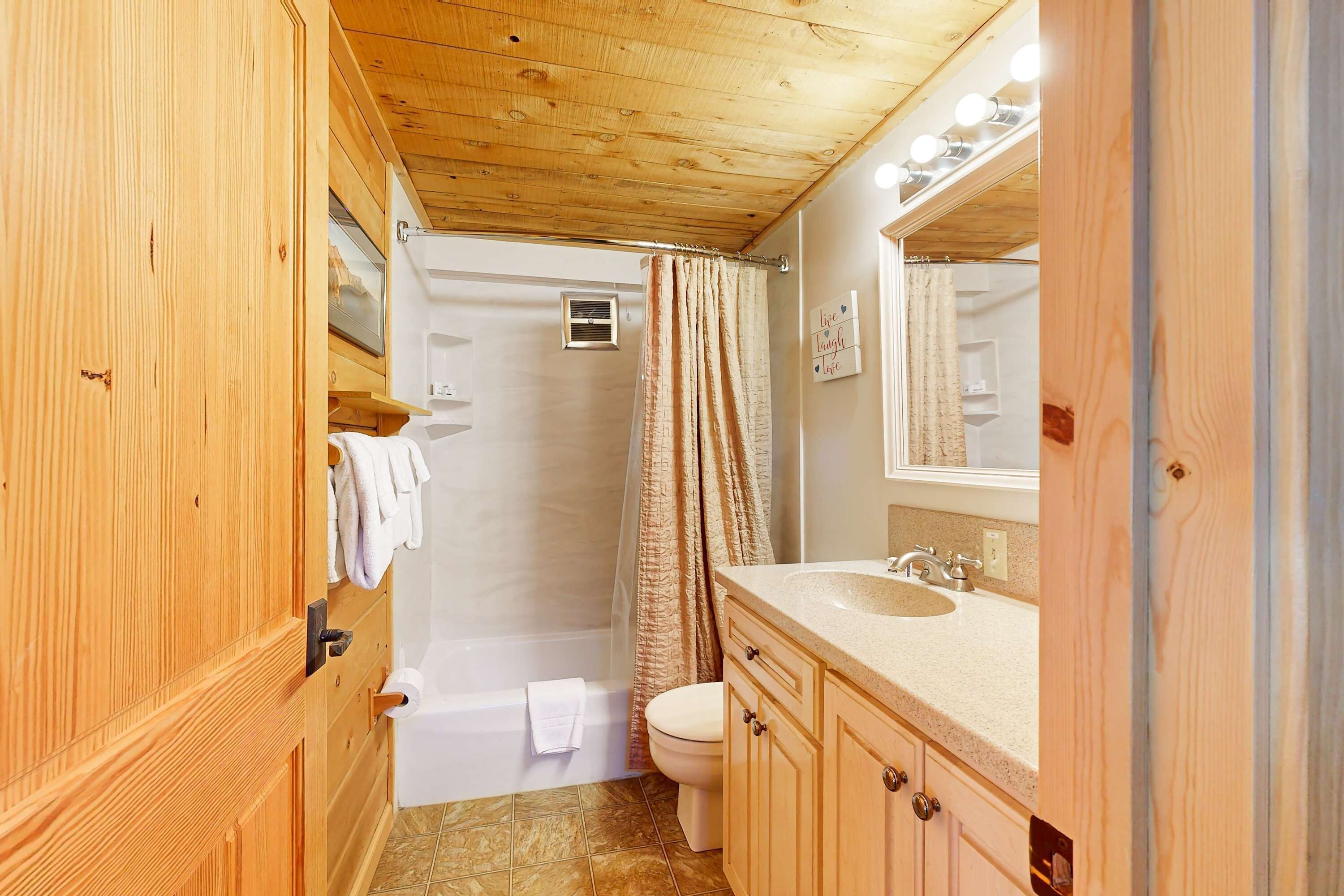 A wooden-paneled bathroom with a bathtub, toilet, vanity, and a mirror.