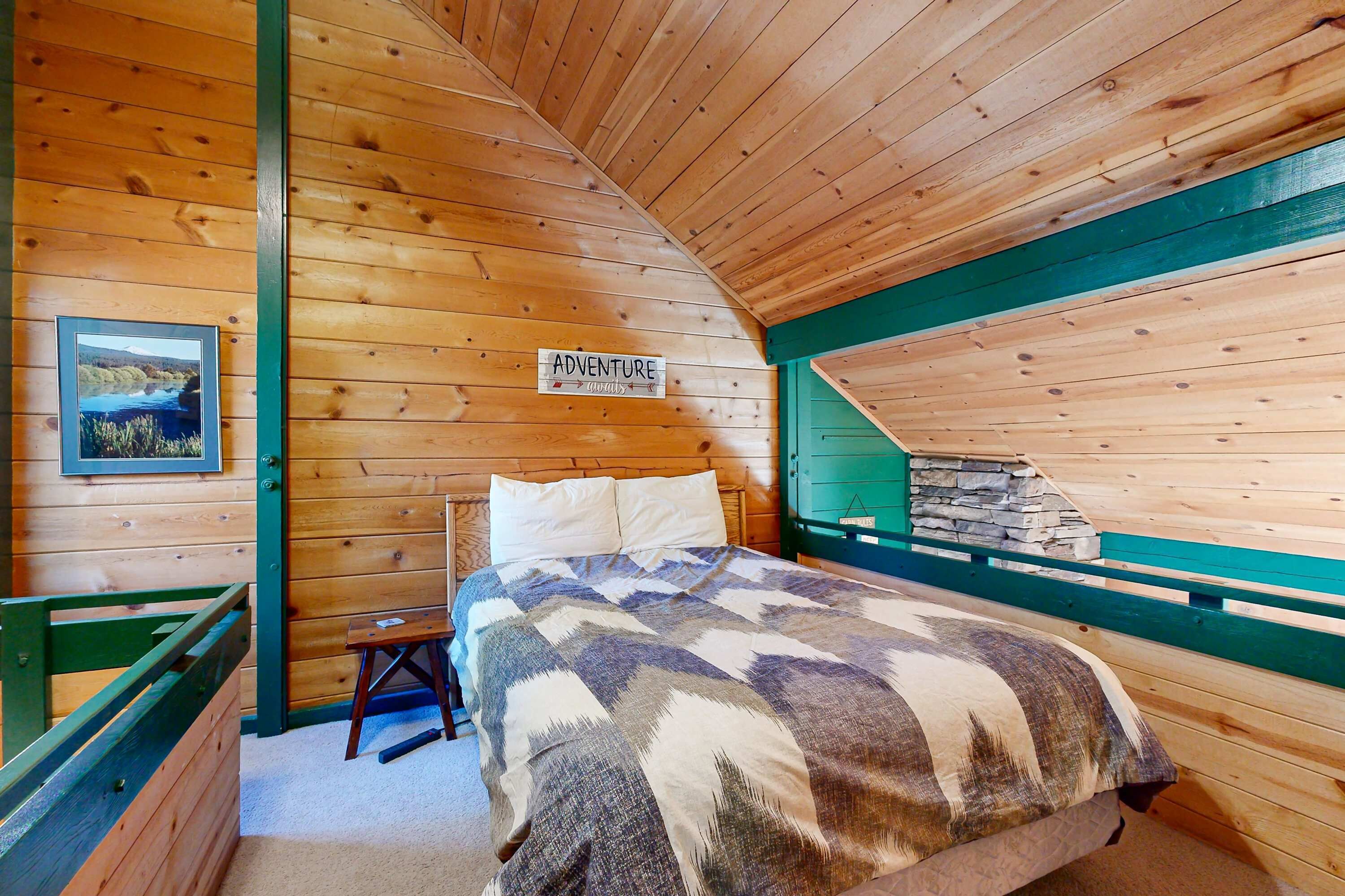 A wooden cabin room with a bed, a framed picture, and a sign that says 'ADVENTURE'.