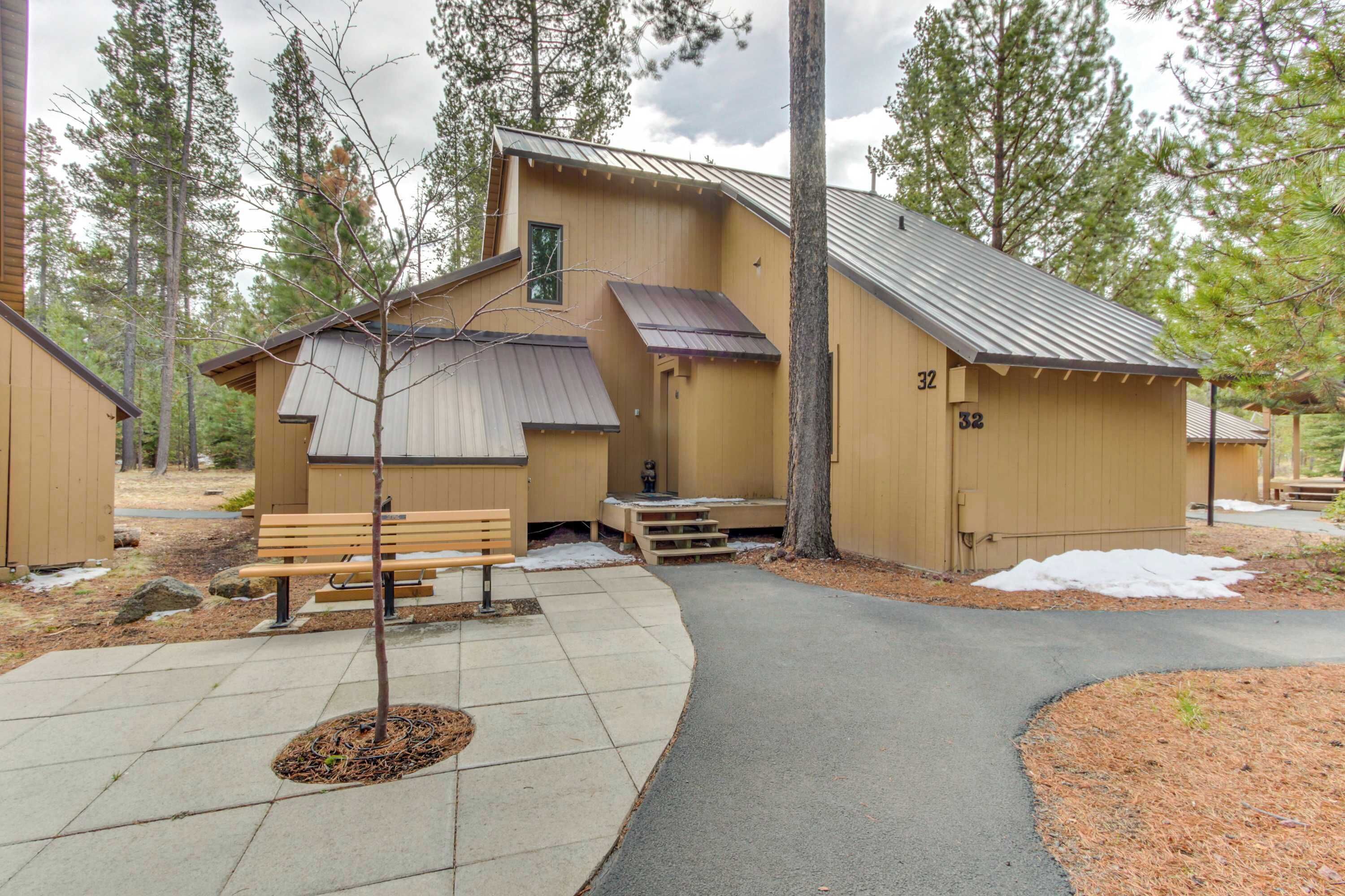 A wooden cabin with a sloped roof, a bench outside, and a paved walkway.