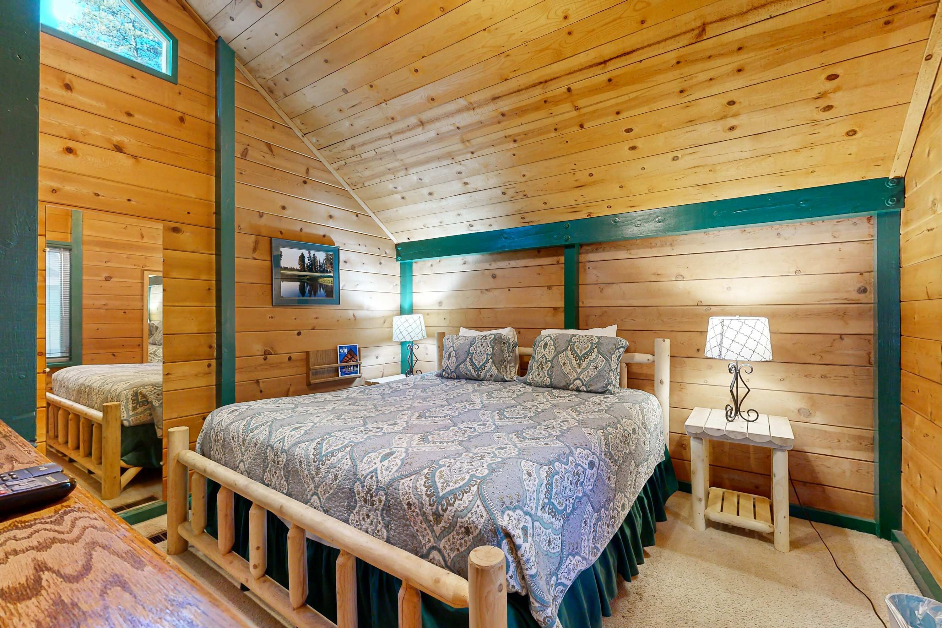 A wooden cabin bedroom with a bed, bedside tables, a lamp, and a framed picture on the wall.