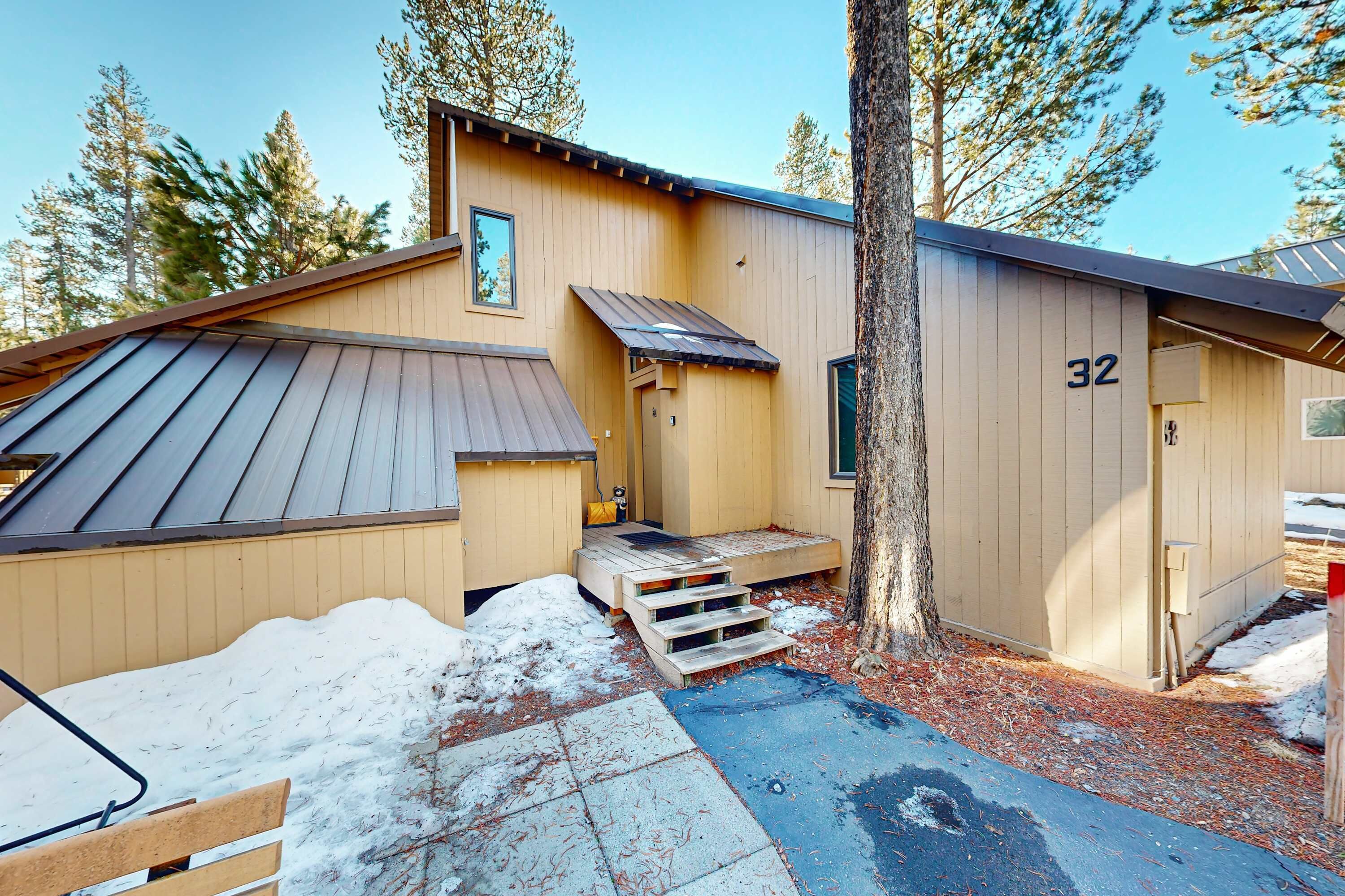 A wooden cabin with a metal roof, a number '32' on the side, and a small porch with steps leading to the door.
